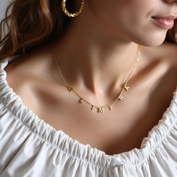 Gold letter necklace spelling 'Glimira,' styled with off-shoulder outfit for a sophisticated and timeless look.